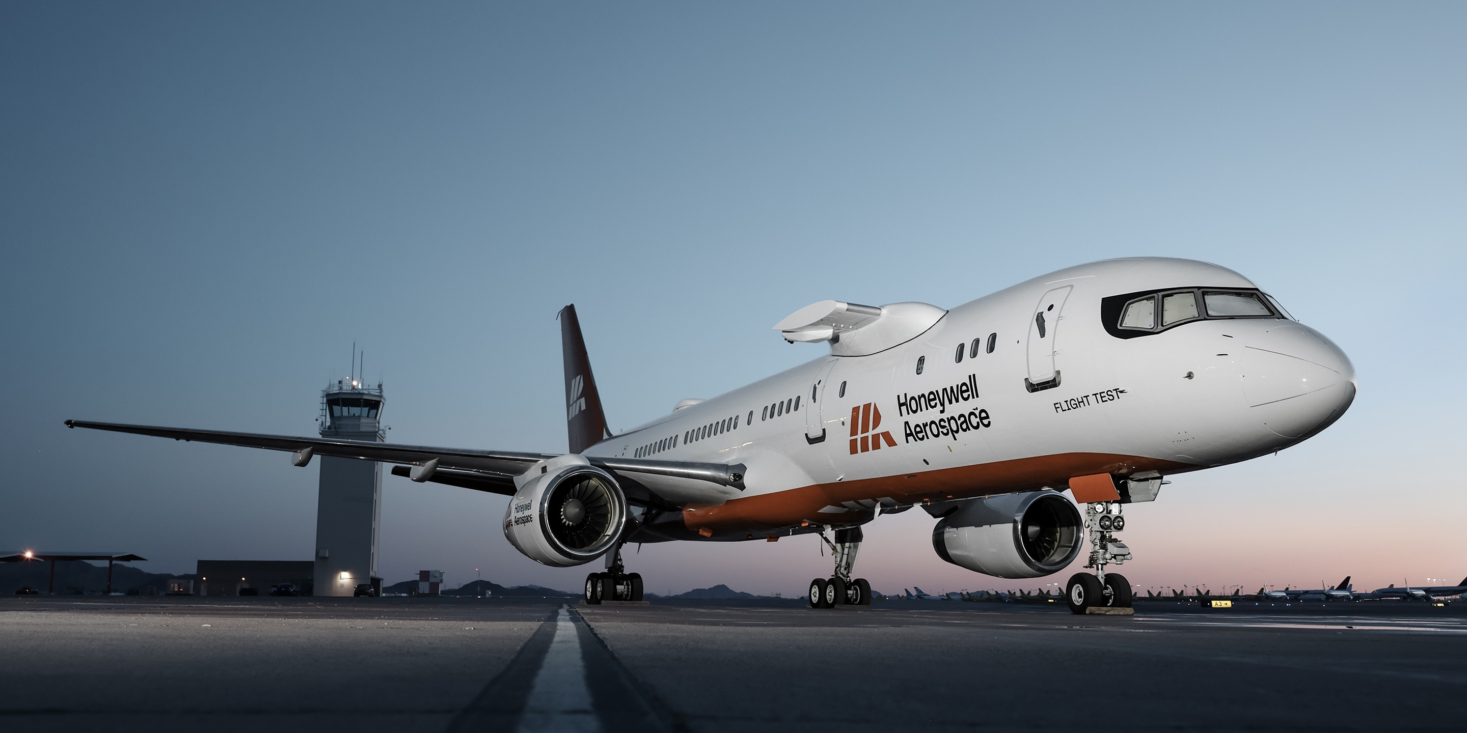 Wide shot of branded jet on tarmac near control tower with soft evening light, representing flight testing and aviation engineering.