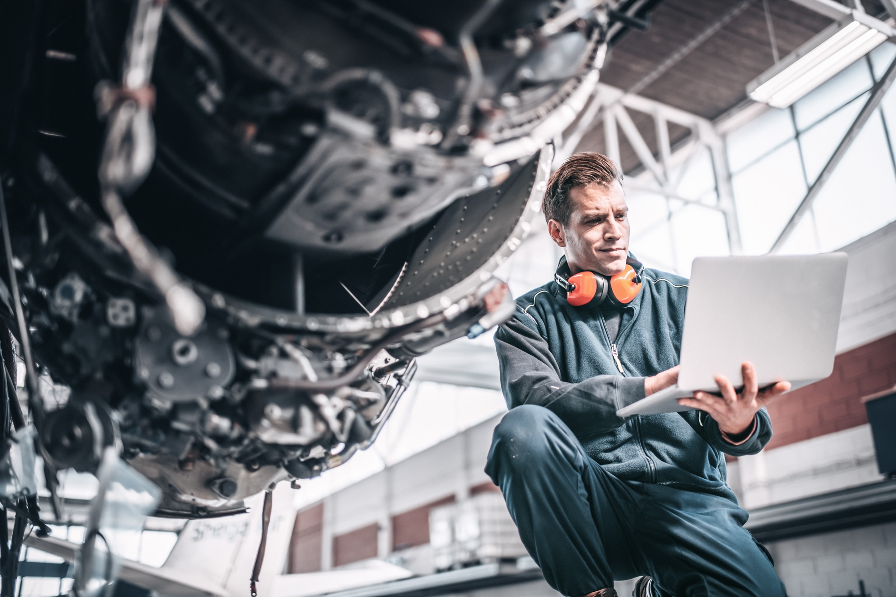 Technician seated beneath aircraft structure working on laptop